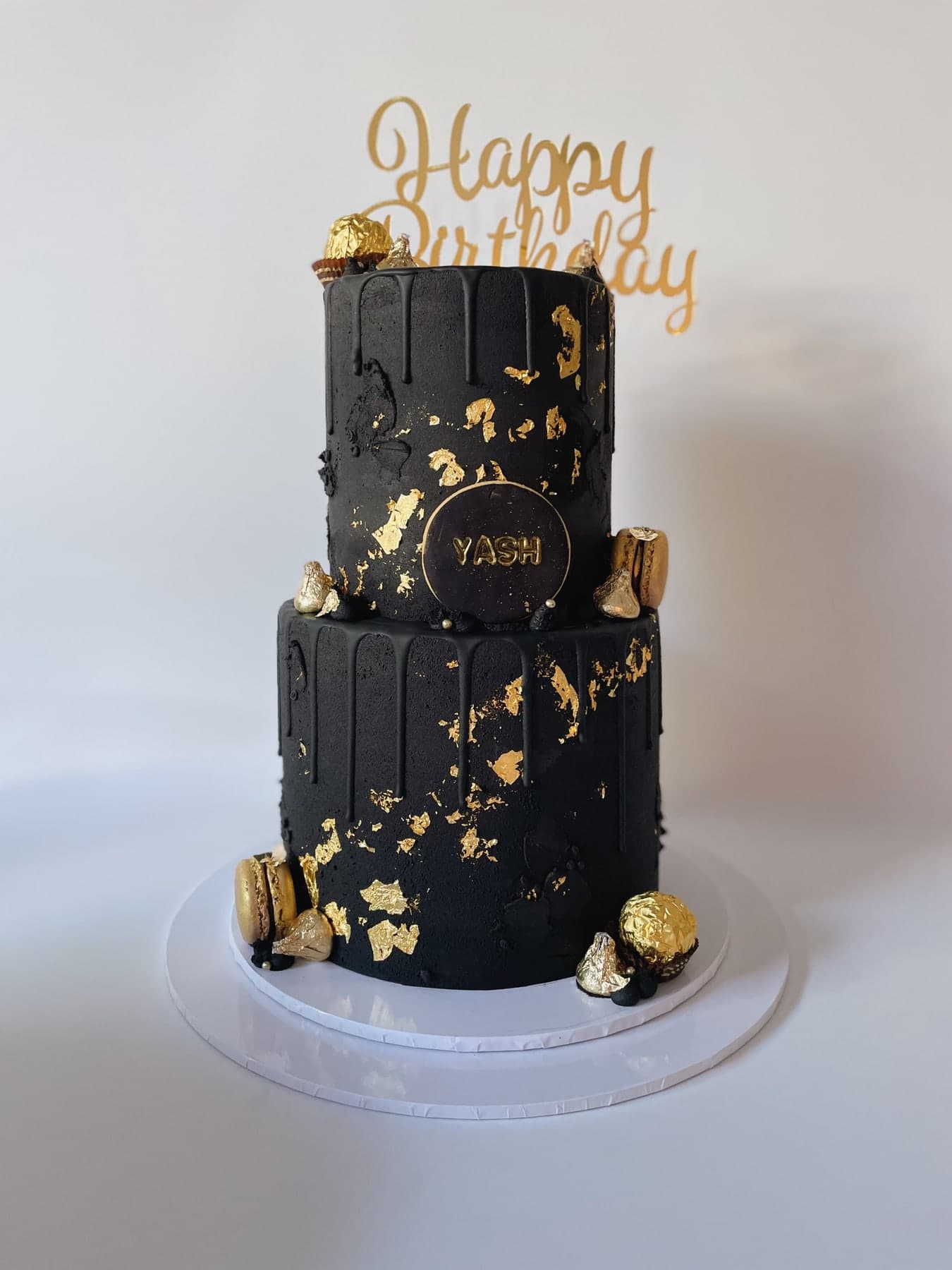 A two-tier cake in matte black with gold leaf across the seam and a dripping gold glaze.