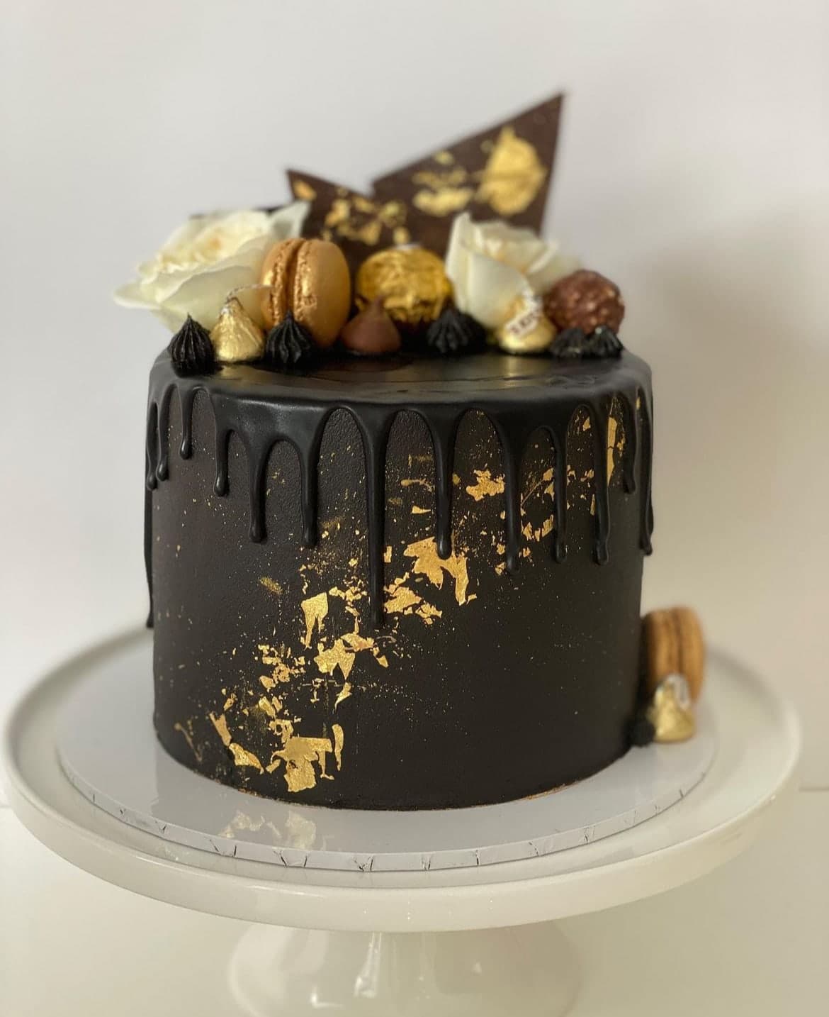 A black chocolate drip cake finished with real gold leaf, white roses and gold macarons.