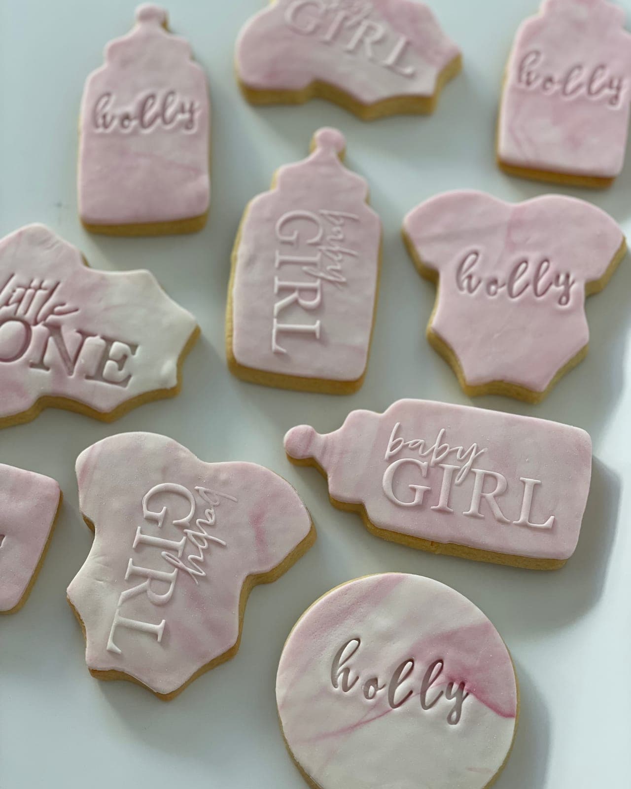 Bottle, onesie and round cookies topped with pink marbled icing and embossed with baby-girl messages.